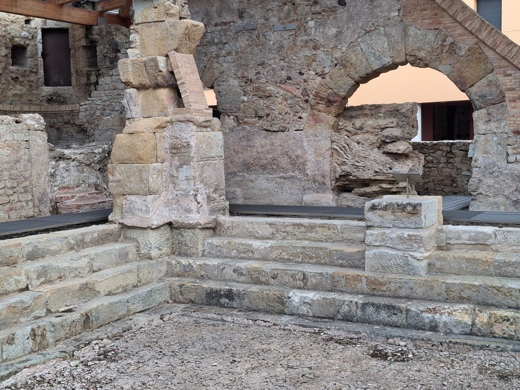 Ruins of an ancient stone structure featuring an archway and a staircase, with weathered stones and brick elements.