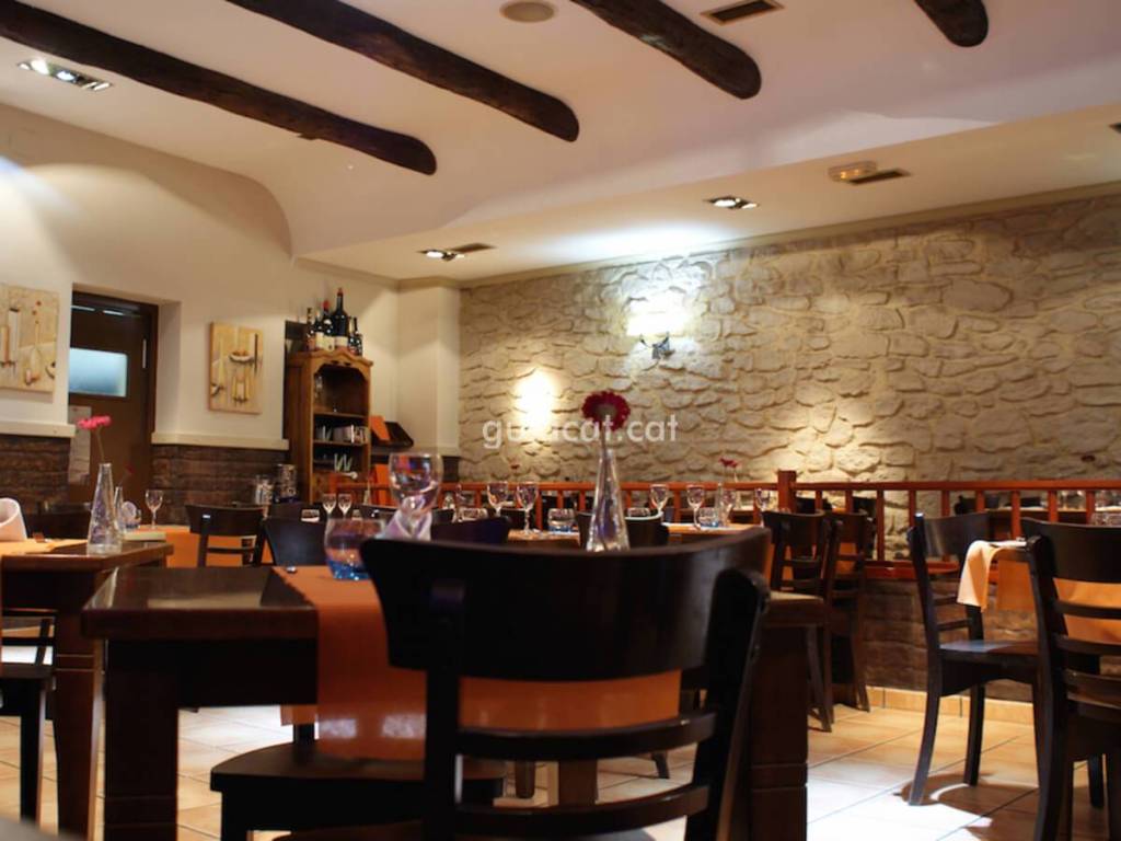 Interior view of a cozy restaurant featuring wooden beams, stone walls, and tables set with glasses and flowers.